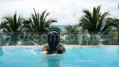 亚洲女人从游泳池下面跳起来，在游泳池里游泳和放松，背景是棕榈树热带海滩。