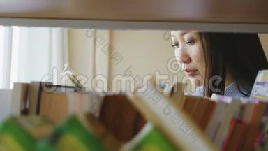 美丽的亚洲严肃的女学生站在书架旁，拿着教科书的大轻图书馆里的书