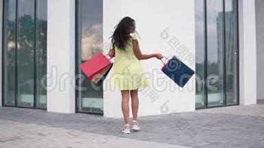 漂亮的女孩模特穿着一件长裙，手里拿着彩色袋子购物后。 慢动作。 高清高清