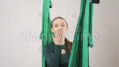 年轻的女人坐在<strong>吊床</strong>上微笑，并发出一个空气亲吻。 空中航空飞行健身教练训练。 冥想，和谐