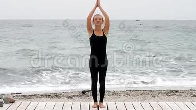 年轻女子在夏天早上在海边<strong>做瑜伽</strong>。 年轻女子在<strong>做瑜伽</strong>和看相机