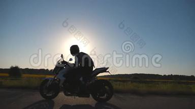 戴头盔的人骑着摩托车在高速公路上，背景是太阳耀斑。 驾驶摩托车的摩托车