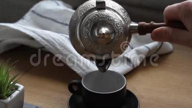 一个男人用双手把咖啡从<strong>水壶</strong>里倒入一个<strong>小</strong>杯子里，喝咖啡