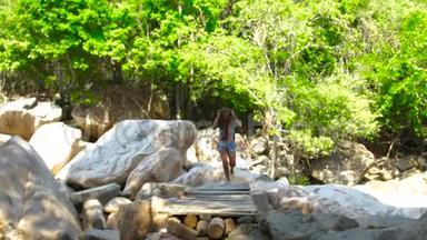 夏季徒步旅行时，游客妇女在山河上的桥上散步。 在热带河桥上散步的年轻女子