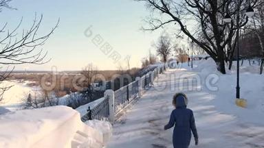穿着<strong>蓝色羽绒服</strong>的年轻女子，带着毛皮罩在冬季公园散步。 后景。
