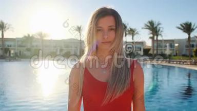 微笑的年轻女孩的肖像，看着相机。 漂亮的女人穿着红色泳衣，在蓝色游泳池附近的热泳池里