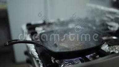 一个厨师在一家餐馆的厨房里，用热的烤炉和牛排煎。 厨师把牛排翻过来。