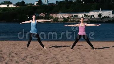 两个女人在城市河边的沙滩上做瑜伽。 日出时美丽的城市景色。 特里科纳桑·乌蒂哈的姿势。