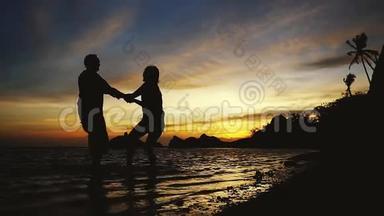 年轻幸福夫妇的剪影在<strong>令人惊叹</strong>的日落时分手牵手旋转，慢动作。 1920x1080