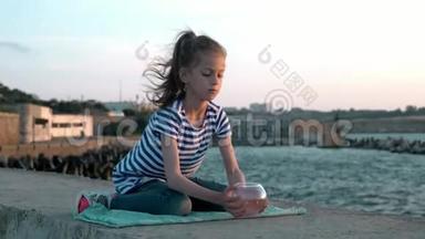 小女孩坐在背景城市码头的海景日落。吃小鱼缸，看小鱼。 概念再现