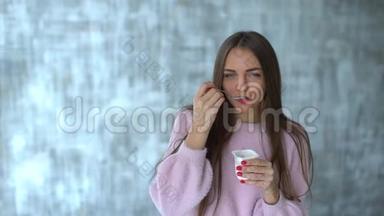 女人吃酸奶。 慢动作。 漂亮的年轻女人吃酸奶。 节食的年轻女人吃白色酸奶。 可爱