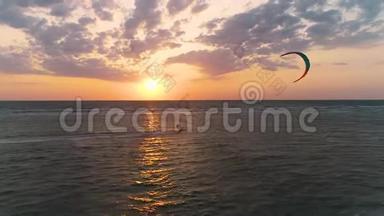 一个美丽的日落在海上，一个风筝手控制着一个训练风筝，从海滩上飘过