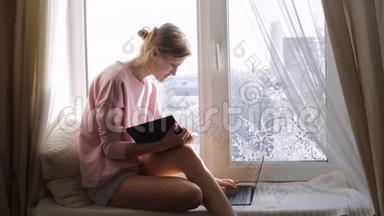 一个拿着记事本的年轻女人坐在窗台上用电脑
