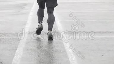 运动鞋跑步者腿的慢动作镜头。 男运动员在户外慢跑。 多雨的单跑道