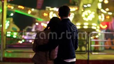 一对夫妇的剪影，站在镜头前，看着游乐园里的景点旋转。 情人