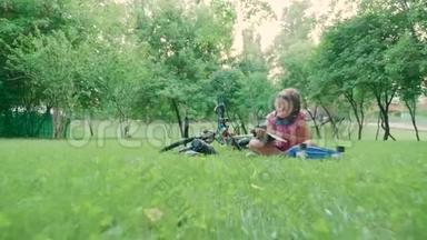可爱的女孩坐在草地上在公园里读一本好书
