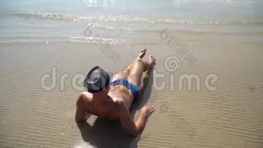 夏天的生活方式视频，漂亮的年轻晒黑的男人戴着帽子。 享受生活，坐在海滩上，旅行的时间