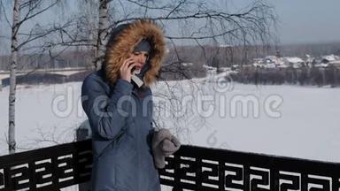 穿着蓝色羽绒服的女人在冬季公园打电话给她的手机。