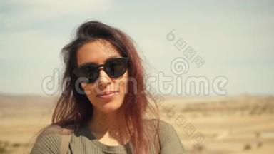 年轻迷人的微笑混合花边女孩肖像在沙漠。 快乐的女游客在镜头前摇摆，在风中摇摆。