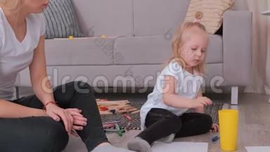 小可爱的金发女孩在和她迷人的妈妈坐在沙发附近画画后，戴上了玻璃毛毡笔。