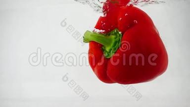 一个新鲜的红铃状甜椒掉进水中，在白色的背景上溅起泡泡