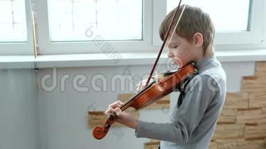 拉小提琴。 七岁的男孩在窗户附近拉小提琴。 侧视。
