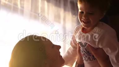 妈妈把小婴儿抱在靠近窗户的房子的手里。 阳光透过窗户。 欢笑和欢乐