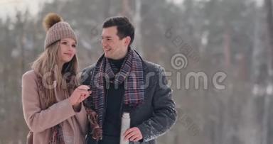 情侣在冬天的森林里<strong>喝热水</strong>瓶里的茶。 冬天公园里穿外套的时髦男女