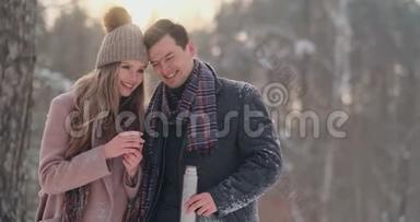 情侣在冬天的森林里<strong>喝热水</strong>瓶里的茶。 冬天公园里穿外套的时髦男女