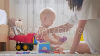 妈妈和她的孩子在室内玩玩具。 在家里在地板上爬行有趣的小男孩。 妈妈和小儿子一起玩