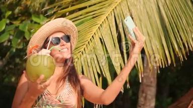 在热带地区用智能<strong>手机</strong>和饮用椰子鸡尾酒<strong>制作</strong>自拍照的年轻混血女游客