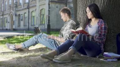 亚洲女孩在<strong>树下看书</strong>，看着男人用笔记本电脑，害羞