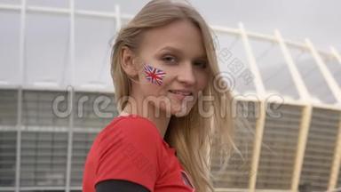 英国一个金发足球迷的年轻女孩，微笑着，像标志一样展示，冠军概念，体育场在