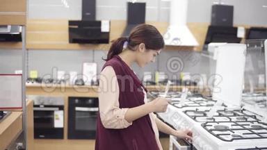 年轻女孩在五金店里寻找完美的炊具。 她检查价格，转动燃烧器按钮打开烤箱