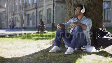 年轻人戴着耳机，听着音乐坐在树下，赞叹不已