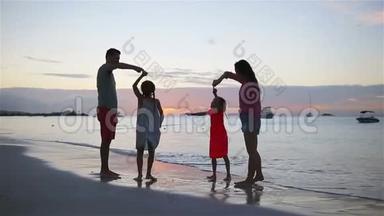 父母和两个孩子在日落时在海滩上玩得很开心。 四口之家相爱，<strong>幸福</strong>美好..