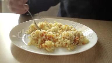一个男人在家里的一张木桌上用一个叉子和一个白色盘子里的鸡肉吃米饭。