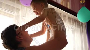 年轻的父亲在玩婴儿，把他抱在我的怀里，扔了起来。 <strong>阳光透过窗户</strong>。 欢笑和欢乐