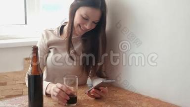 年轻漂亮的女孩在手机上通过社交网络上的磁带，喝啤酒。