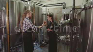 酿酒工人看着玻璃管里刚做的啤酒，讨论着它。 男女啤酒制造商在