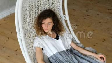穿亚麻布连衣裙的年轻欧洲女孩在阁楼公寓的吊床上摇摆。 美丽的女人躺在吊床上