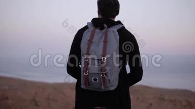 一个背着背包的人独自站在黄昏的沙漠里。 慢动作。 旅行者看着夕阳的天空。 寻找灵感。