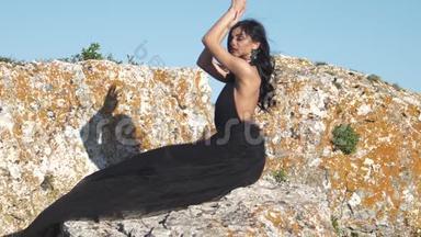 年轻女子坐在石头上，举起双手，摆姿势拍照