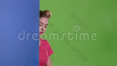 女孩从一块蓝色的木板后面窥视，并显示一个OK。绿色屏幕。 慢动作