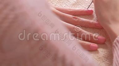 女人用小流苏把第二层粉红色的紫胶涂在她的指甲上。 特写双手。