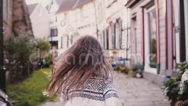 小女孩看着镜头，在铺好的路上奔跑。 后景。 慢动作。 可爱的欧洲孩子在老街上跑步。