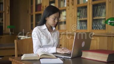 漂亮的女人<strong>正在</strong>使用笔记本电脑，<strong>看书</strong>坐在图书馆的桌子上。