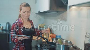 女人妈妈在厨房做饭的概念。 在平底锅里煮汤，看看数字平板电脑上的食谱。 女孩