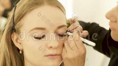 女化妆师用闭眼触摸黑色<strong>眼线</strong>到眼睑时尚模特。 使用佩伊利纳关闭面罩