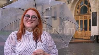 戴眼镜的胖姜女站在雨天，撑着伞，看着镜头，微笑着，继续前进